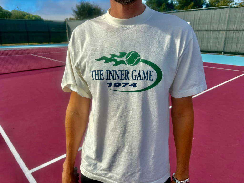 Man wearing The Inner Game 1974 tennis graphic tee on a tennis court